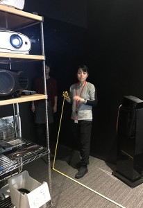プロジェクター投写距離をメジャーで測る細井