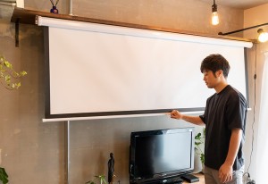プロジェクター用のスクリーンを下ろす旦那様